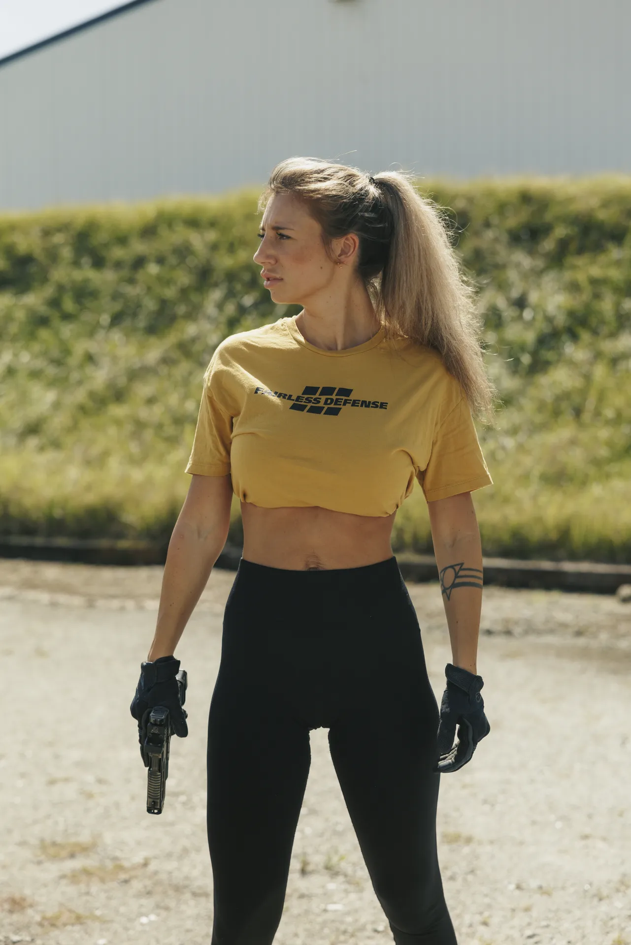 Person wearing a yellow Fairless Defense crop top holding a firearm at an outdoor range